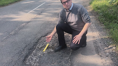 Henry Vann kneeling beside a large pothole